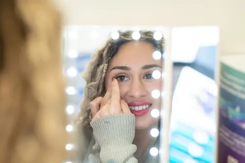 A patient inserting a contact lens at a lighted mirror